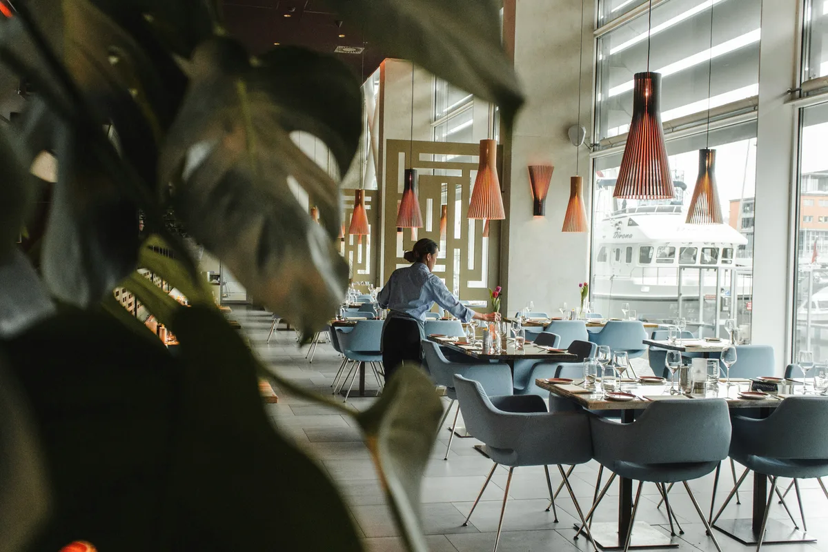 A member of restaurant staff preparing tables for service in a bright dining room